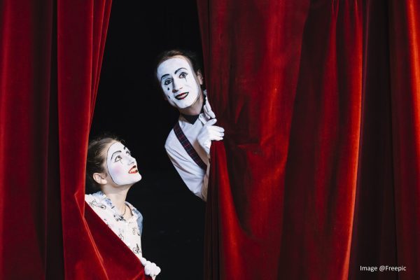 smiling-female-mime-artist-looking-at-male-mime-artist-peeking-from-curtain